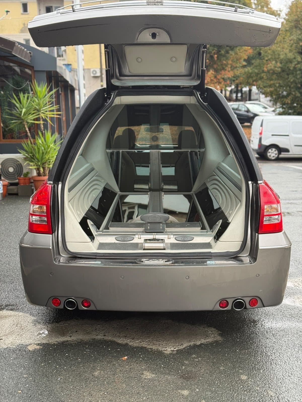 Autospeciala funerară cu hayonul ridicat, pregătită pentru ceremonie